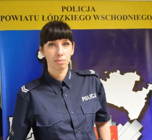 Policjantka w granatowym mundurze stoi ustawiona na tle kolorowego baneru.