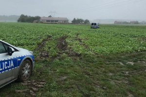 Zakopany samochód w polu i obok niego stoi radiowóz.