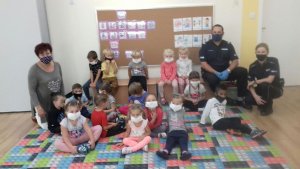 Policjanci siedzą z dziećmi na dywanie.