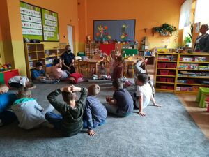 Dzielnicowi rozmawiają z dziećmi, które siedzą w ławkach i na dywanie.