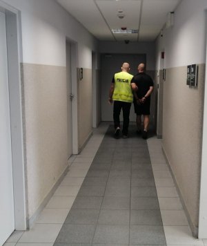 Policjant prowadzi zatrzymanego mężczyznę.