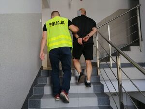 Policjant prowadzi zatrzymanego mężczyznę.