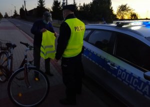 Dzielnicowy rozdaje kamizelki odblaskowe mieszkańcom.