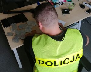 Policjant siedzi przy biurku i przesłuchuje zatrzymanego, który siedzi przed nim.