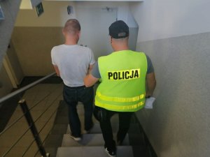 Policjant prowadzi zatrzymanego mężczyznę.