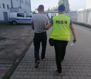Policjant prowadzi zatrzymanego mężczyznę.