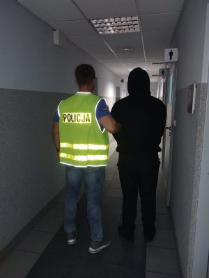 Policjant prowadzi zatrzymanego mężczyznę.