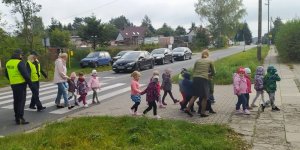 Policjanci przechodzą z dziećmi przez jezdnię na przejściu dla pieszych.