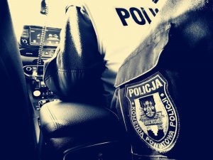 naszywka na rękawie munduru z napisem Komenda Powiatowa Policji powiatu łódzkiego wschodniego, w tle siedzi tyłem policjant w radiowozie w kamizelce z napisem POLICJA