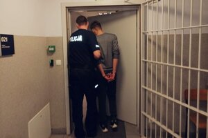 Korytarz komendy, policjant prowadzi zatrzymanego mężczyznę.