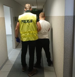 Nieumundurowany policjant w żółtej kamizelce prowadzi zatrzymanego mężczyznę