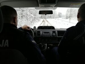 Dwóch umundurowanych policjantów jedzie radiowozem zaśnieżonymi drogami.