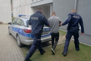 Umundurowani policjanci prowadzą do radiowozu zatrzymanego mężczyznę.