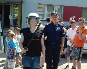umundurowana policjantka stoi przy chłopcu i grupie uczniów, chłopiec ma na sobie policyjne umundurowanie
