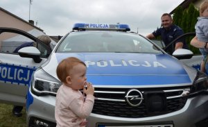 dziecko stoi przy radiowozie a przy drzwiach samochodu stoi umundurowany policjant