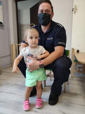 umundurowany policjant w maseczce na twarzy stoi przy dziecku