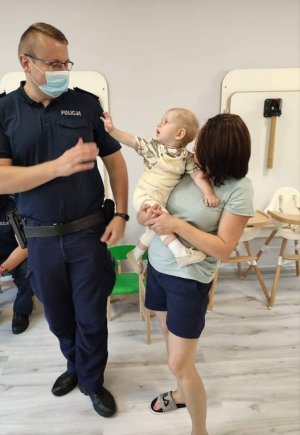 umundurowany policjant w maseczce na twarzy stoi przy dziecku
