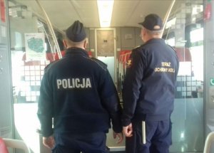 umundurowany policjant i funkcjonariusz służby ochrony kolei są w pociągu i idą przed siebie, odwróceni tyłem