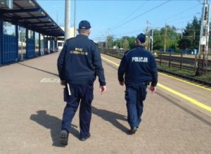 umundurowany policjant i funkcjonariusz służby ochrony kolei idą peronem wzdłuż torów kolejowych