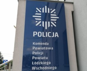 niebieski szyld na ścianie komendy z białymi napisami Policja, poniżej napis  Komenda Powiatowa Policji powiatu łódzkiego wschodniego