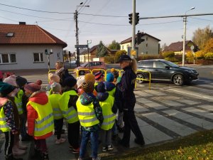 umundurowana policjantka stoi przy grupie dzieci ubranej w odblaskowe kamizelki, tuż przed przejściem dla pieszych