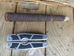 Znaleziony pocisk leży na drewnianej skrzynce, obok niego leży składany scyzoryk.