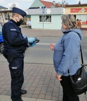 policjant w granatowym mundurze wręcza maseczkę kobiecie