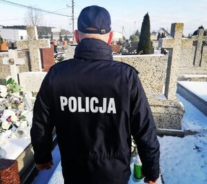 Umundurowany policjant stoi odwrócony tyłem, przed nim są groby.