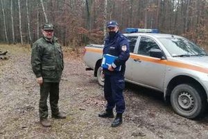 umundurowany policjant i strażnik leśny stoją przy samochodzie służbowym w lesie