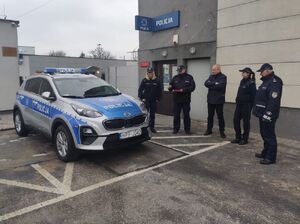 Umundurowani policjanci i wójt stoją przed budynkiem ,obok nich stoi nowy radiowóz.