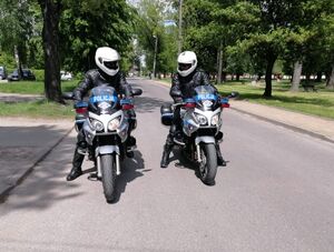 Policjanci w białych kaskach siedzą na motocyklach oznakowanych.