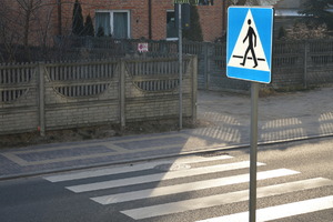 Przejście dla pieszych, zebra namalowane białe pasy na jezdni, obok stoi znak pionowy niebieski z idącym człowiekiem po pasach
