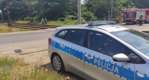 Radiowóz policyjny stoi zaparkowany przy torach kolejowych.