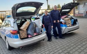 Policjantka z policjantem stoją przy zapakowanych bagażnikach radiowozów.