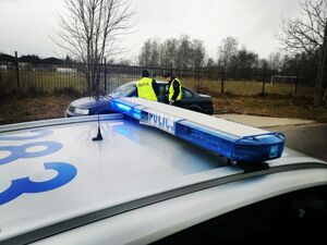 Umundurowani policjanci stoją przy granatowym samochodzie.