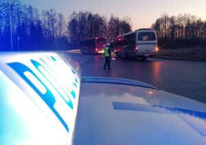 Policjant w białej czapce i żółtej kamizelce stoi na środku drogi i kieruje ruchem.