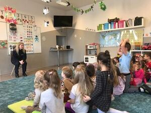 Policjantka w granatowym mundurze mówi do dzieci siedzących przed nią.