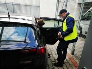 Policjant stoi przy otwartych drzwiach samochodu i patrzy na mężczyznę zatrzymanego, który wsiada do samochodu.