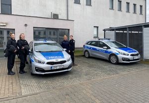 Uczennice w czarnych mundurach stoją przy radiowozie z policjantką.