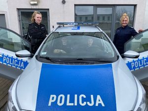 Uczennice w czarnych mundurach stoją przy radiowozie z policjantką.