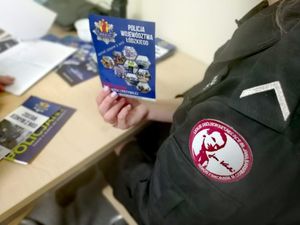 Naszywka na mundurze z  logo liceum na ramieniu uczennicy trzymającej w dłoni ulotki rekrutacyjne do policji.