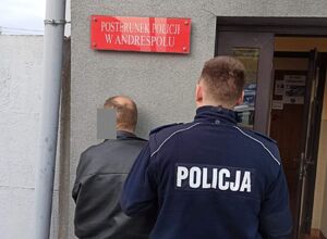 Policjant stoi odwrócony tyłem z zatrzymanym mężczyzną.