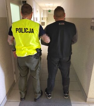 policjant w kamizelce z napisem policja prowadzi zatrzymanego mężczyznę