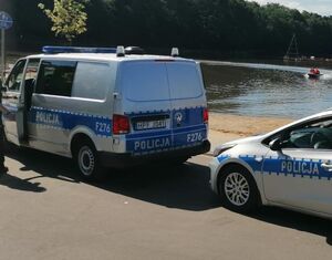 dwa radiowozy stoją zaparkowane jeden za drugim w okolicy zbiornika wodnego i plaży