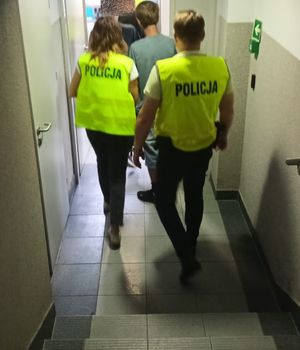 policjanci w żółtych kamizelkach z napisem policja prowadzą zatrzymanego mężczyznę