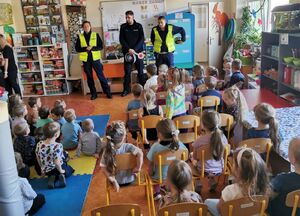 trójka policjantów stoi w sali gdzie na krzesełkach przed nimi siedzi grupa przedszkolaków