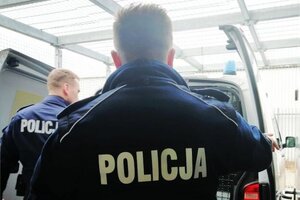 dwóch policjantów stoi przy radiowozie, w którym otworzone są tylne drzwi