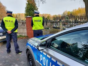 policjanci w białych czapkach na głowie i żółtych kamizelkach z napisem policja stoją przed cmentarzem