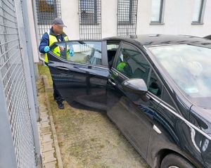 policjant w żółtej kamizelce zamyka tylne drzwi czarnego samochodu
