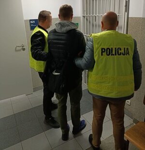 policjanci w żółtych kamizelkach z napisem policja prowadzą zatrzymanego mężczyznę